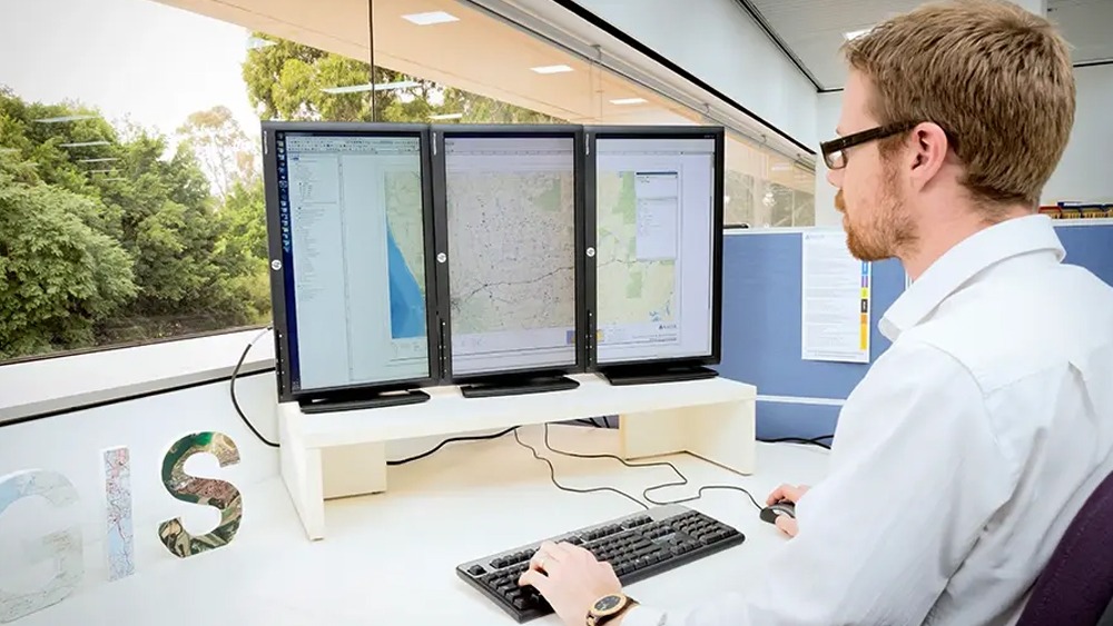 An image of an office worker for Water Corporation looking at three screens with technical information.