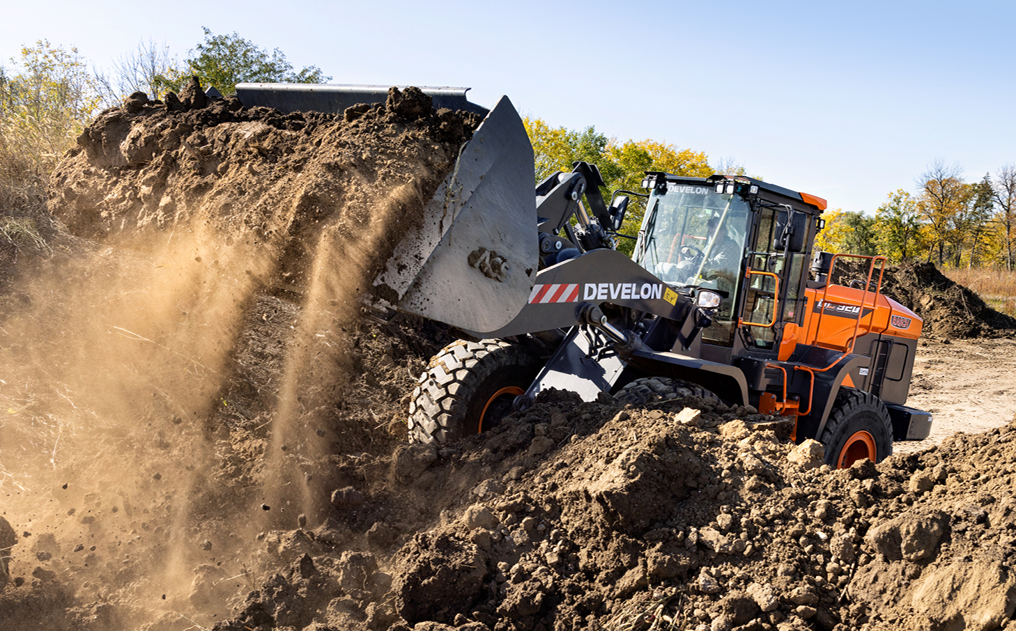 A DEVELON wheel loader dumping a bucket of dirt on a field.
