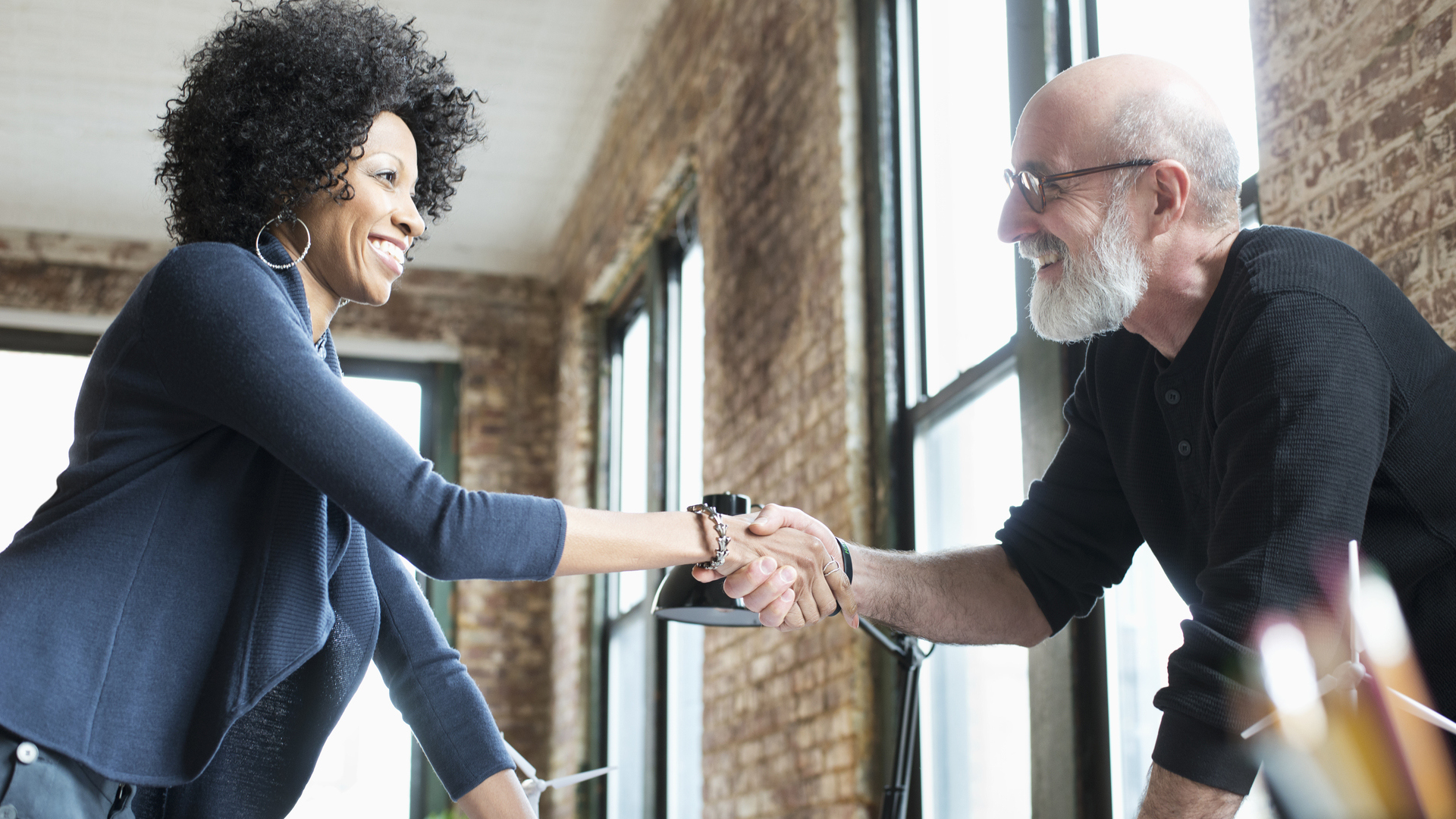 Business people handshaking over blueprints on desk