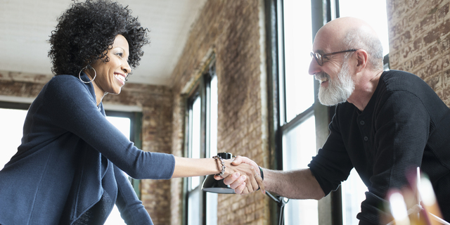 Business people handshaking over blueprints on desk