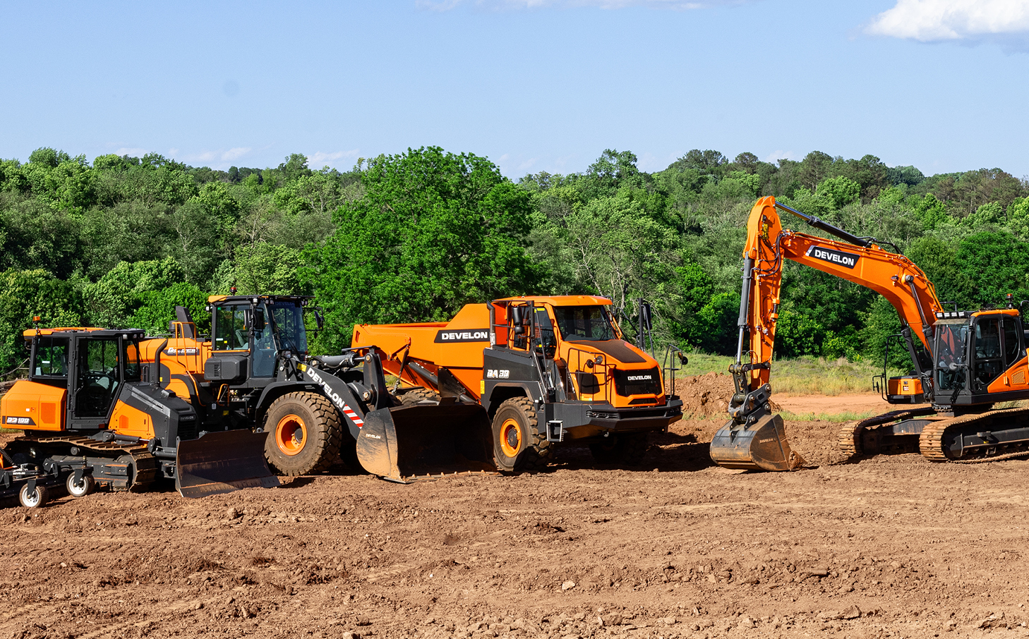 A lineup of DEVELON equipment, including a dozer, wheel loader, ADT and crawler excavator, in front of a tree-lined background in the southeast U.S.