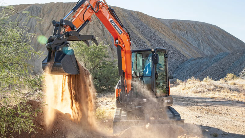 A DEVELON mini excavator dumping dirt on a job site.