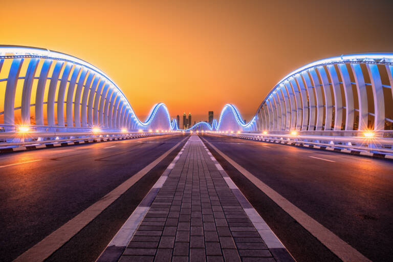 A large bridge lit up by neon lights featuring two opens roads at dusk