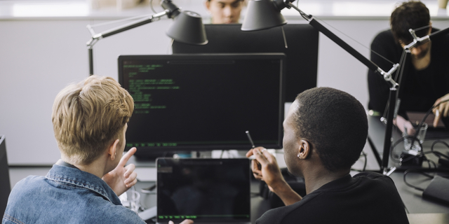 Male computer programmers discussing over codes at desk in office