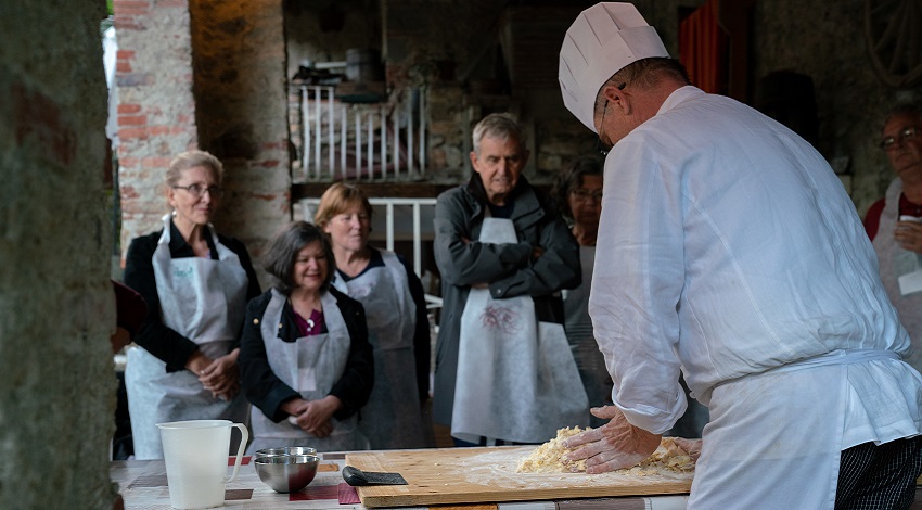 A group of Road Scholars watches a chef prepare food as part of a cooking class