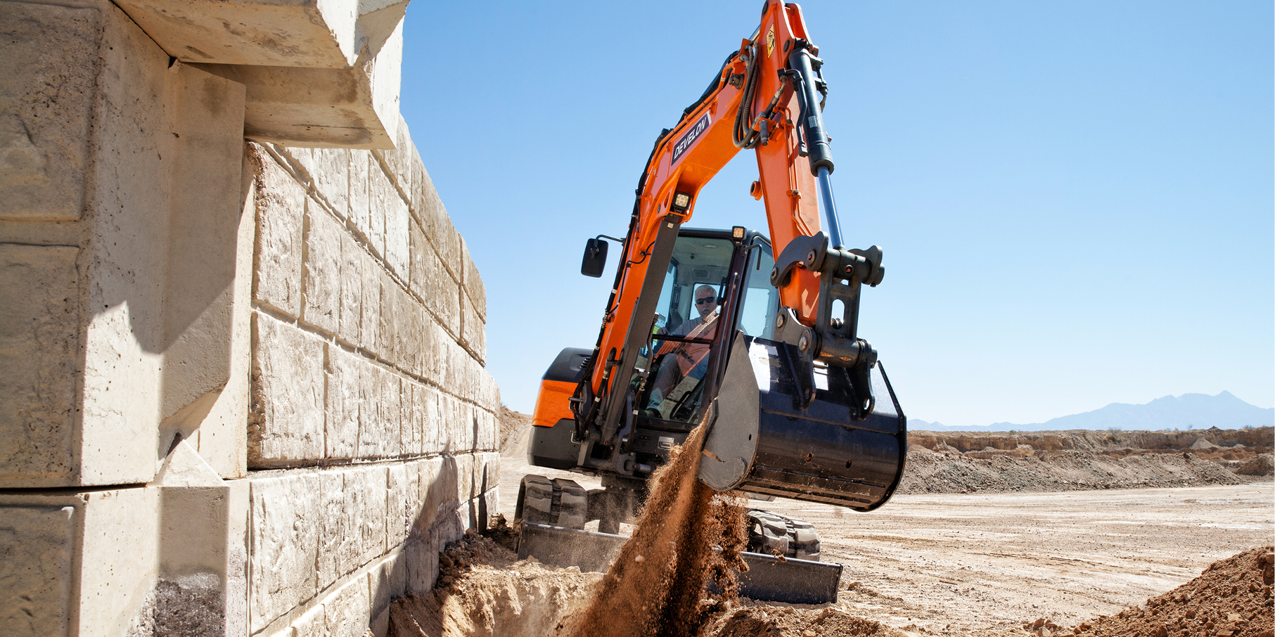 A DEVELON mini excavator works along a wall at a job site.