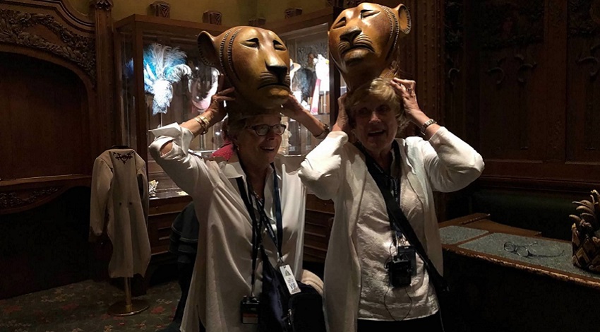 Two women laugh while trying on lion costumes from The Lion King theater production
