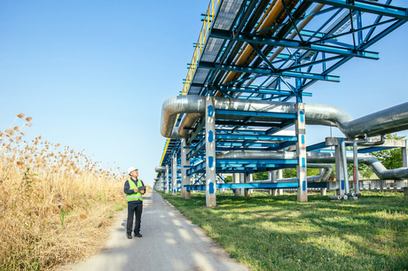 Worker in high-vis inspecting critical infrastructure elevated pipes