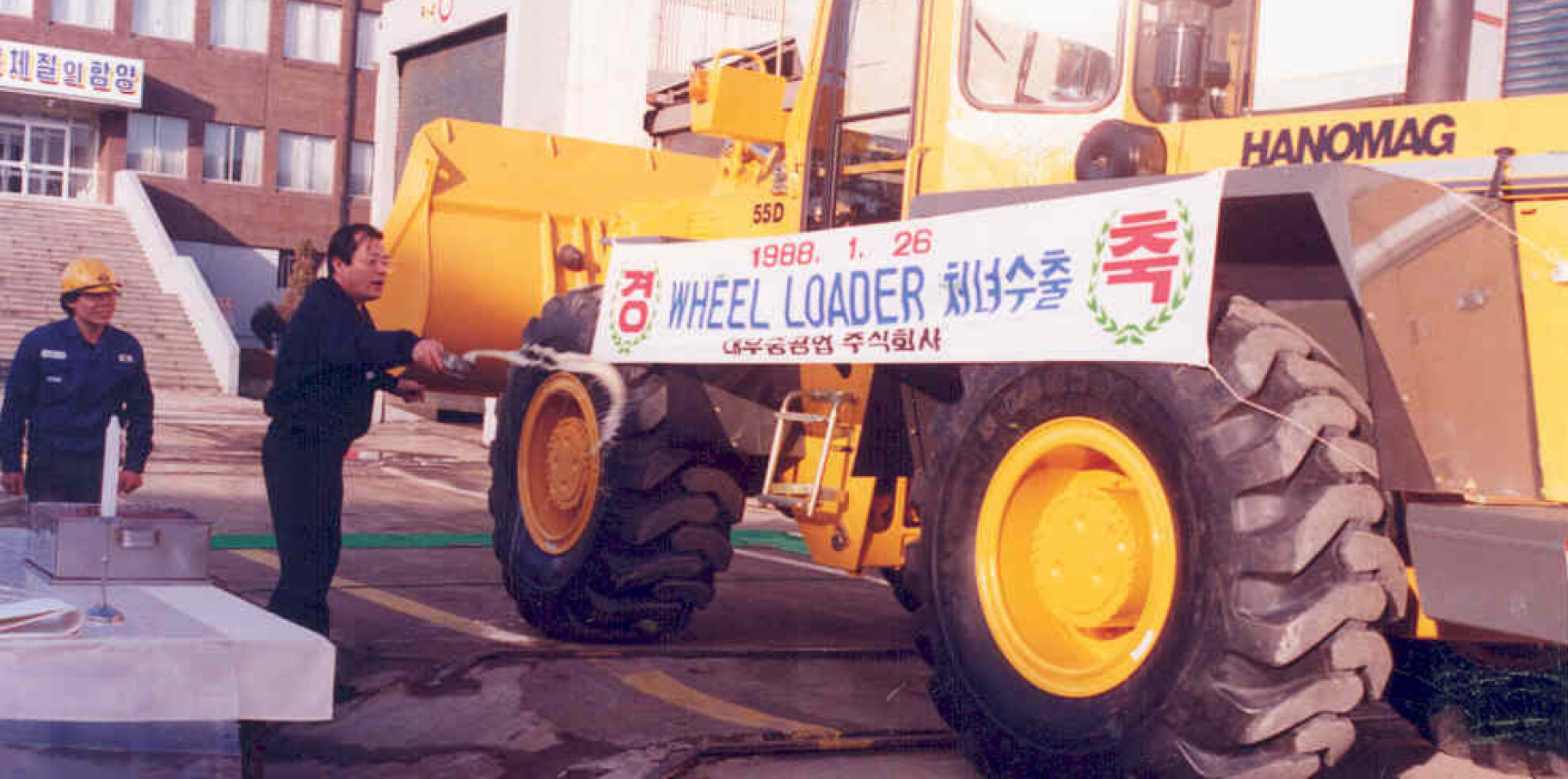 A historical photo of a large wheel loader with a ceremonial banner.