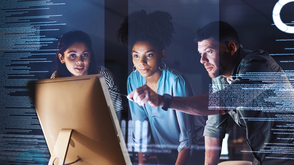 Stock image of three workers looking at Desktop with data