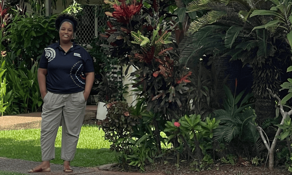 A person standing on a sidewalk in front of a house surrounded by lush greenery and tropical plants.