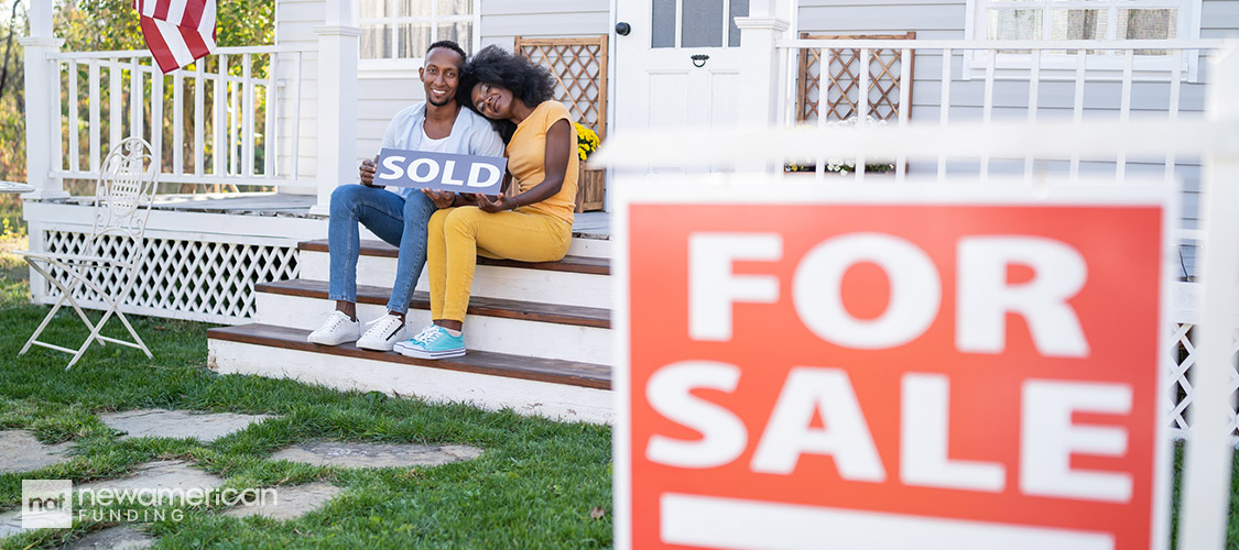 couple sitting on a porch holding a sold sign