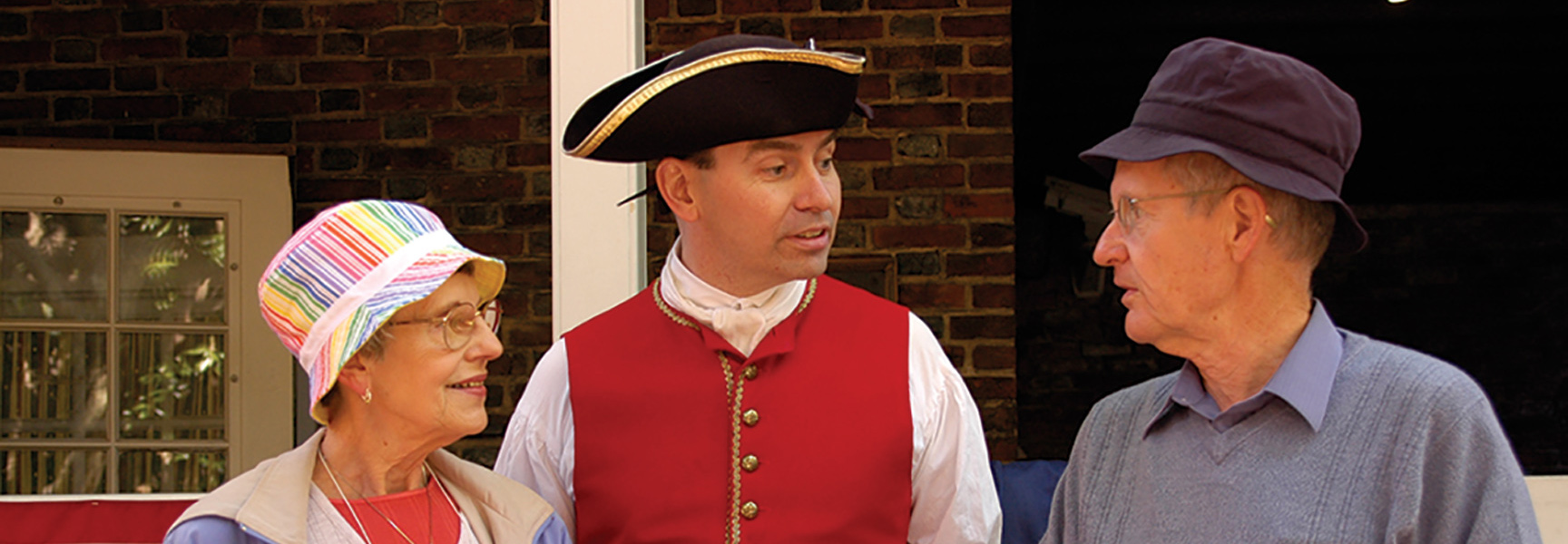 A historical reenactor in a red vest and tricorn hat speaks with an older couple in Philadelphia.
