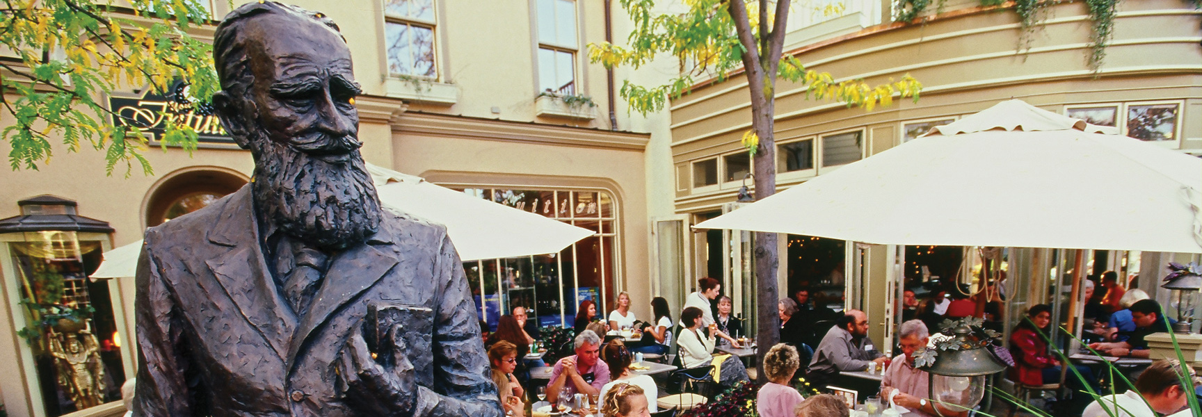 A bronze statue of George Bernard Shaw overlooks a busy outdoor restaurant patio at the Shaw Festival in Ontario.