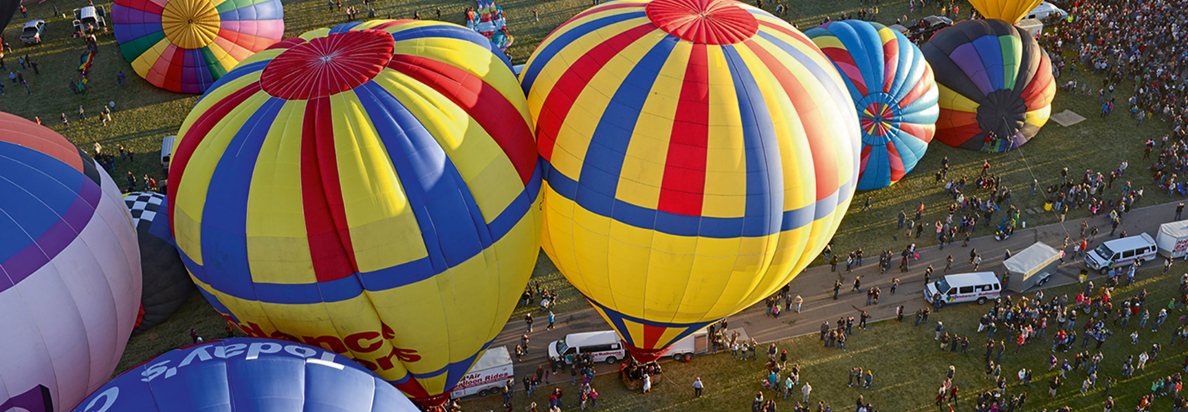 An aerial view of colorful hot air balloons on the ground with crowds of people below at the Albuquerque International Balloon Fiesta in New Mexico.