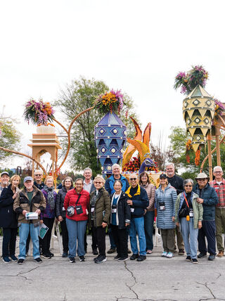 A group of visitors posing in front of a decorated Downey Rose Float Association float at the Rose Parade in Pasadena, California.