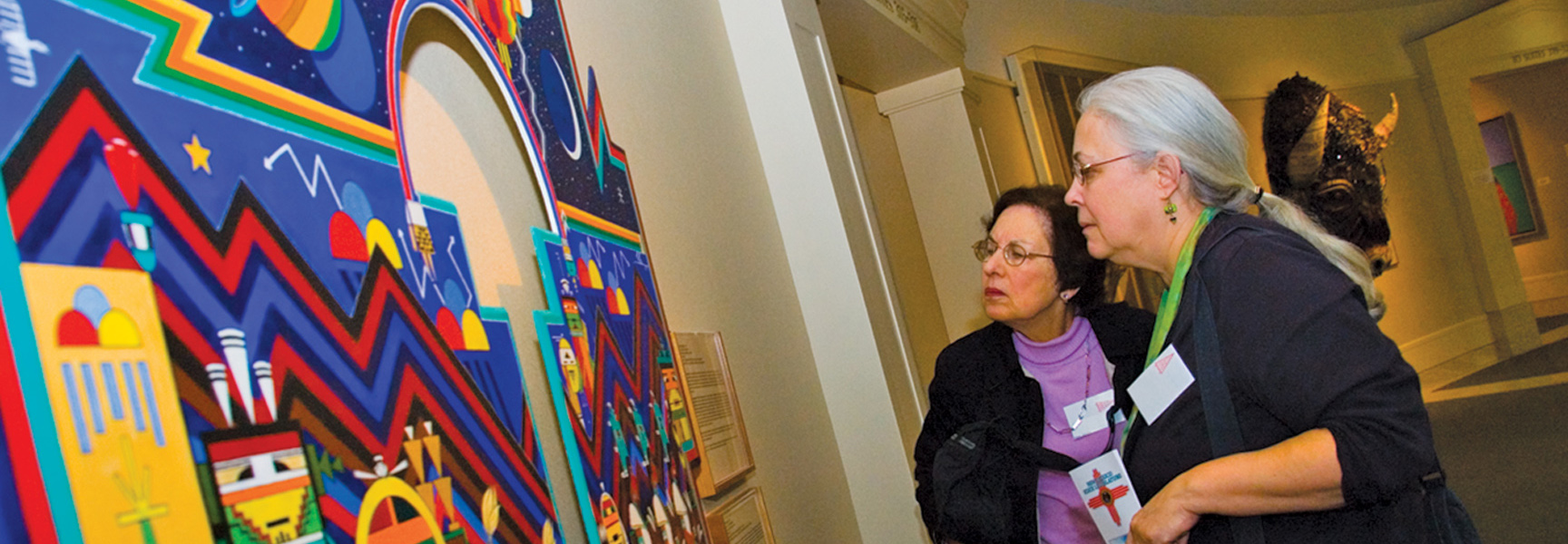 Two women view a large, colorful piece of Indigenous art at a museum in Santa Fe, New Mexico.