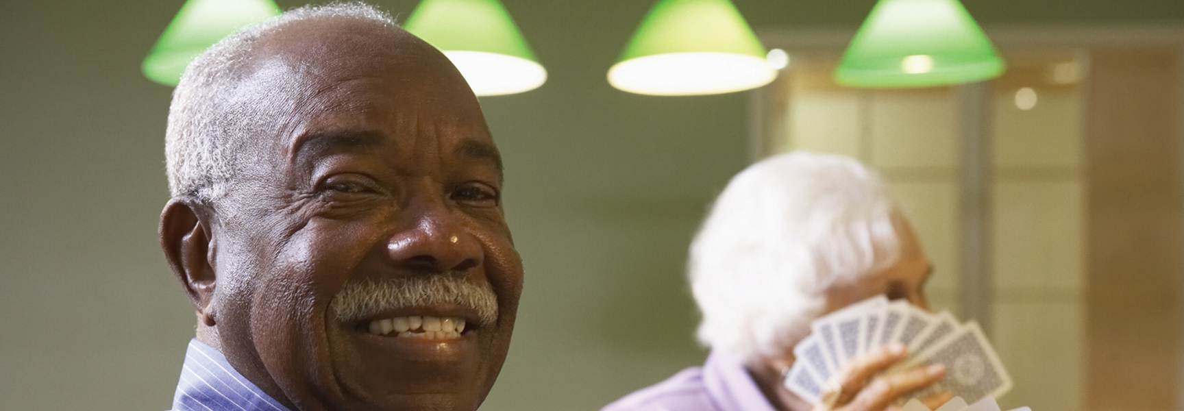 A smiling older man enjoys a game of bridge with another player in the background at the Jekyll Island Club in Georgia.