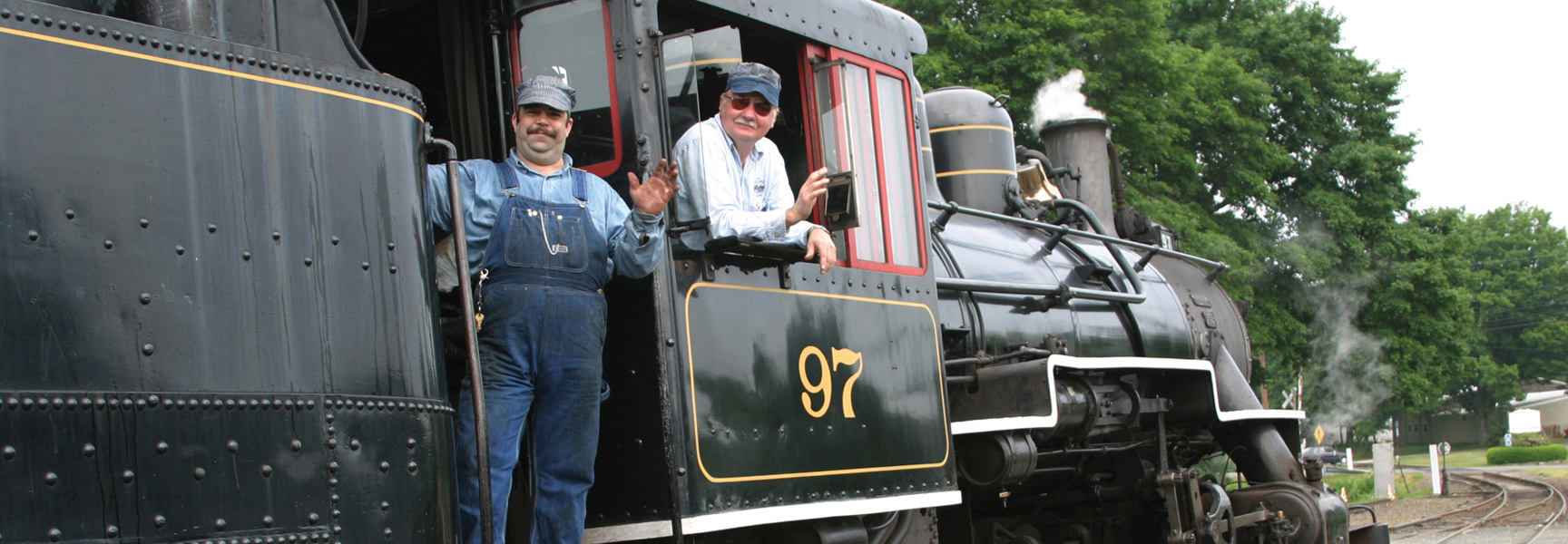 Two conductors wave from the number 97 engine of a vintage steam train in Connecticut or New Hampshire.
