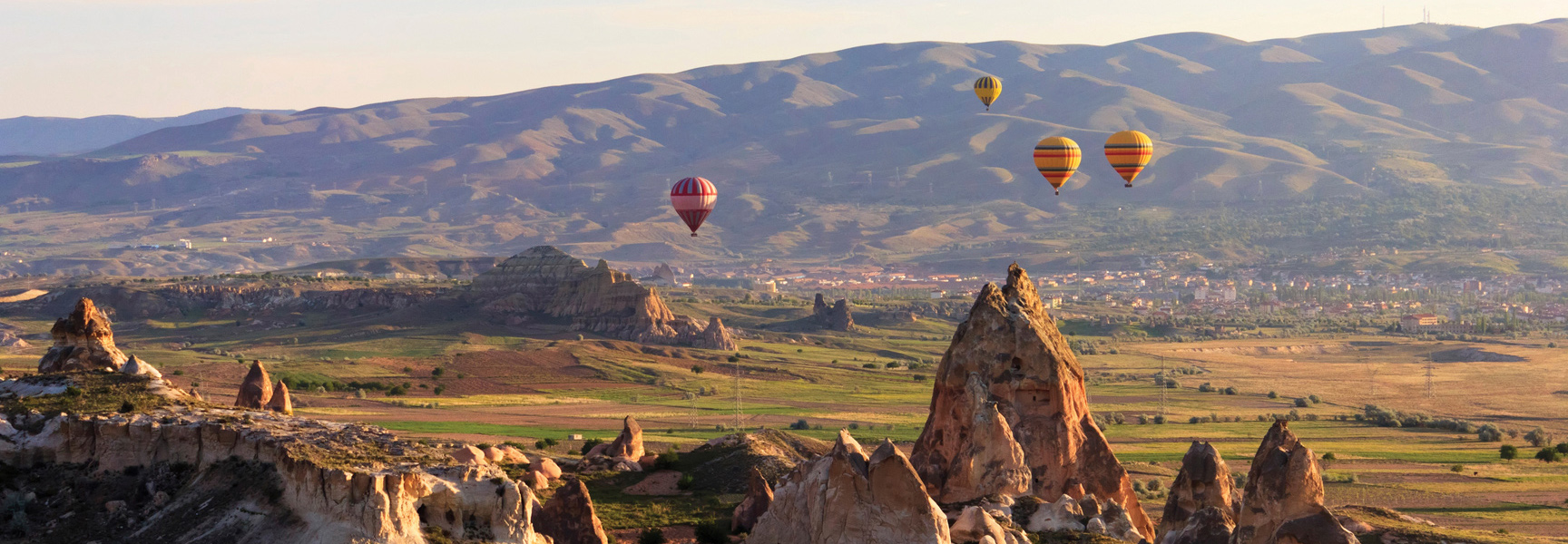 Hot air balloons float over the rocky valleys and unique fairy chimneys of Turkey at sunrise.