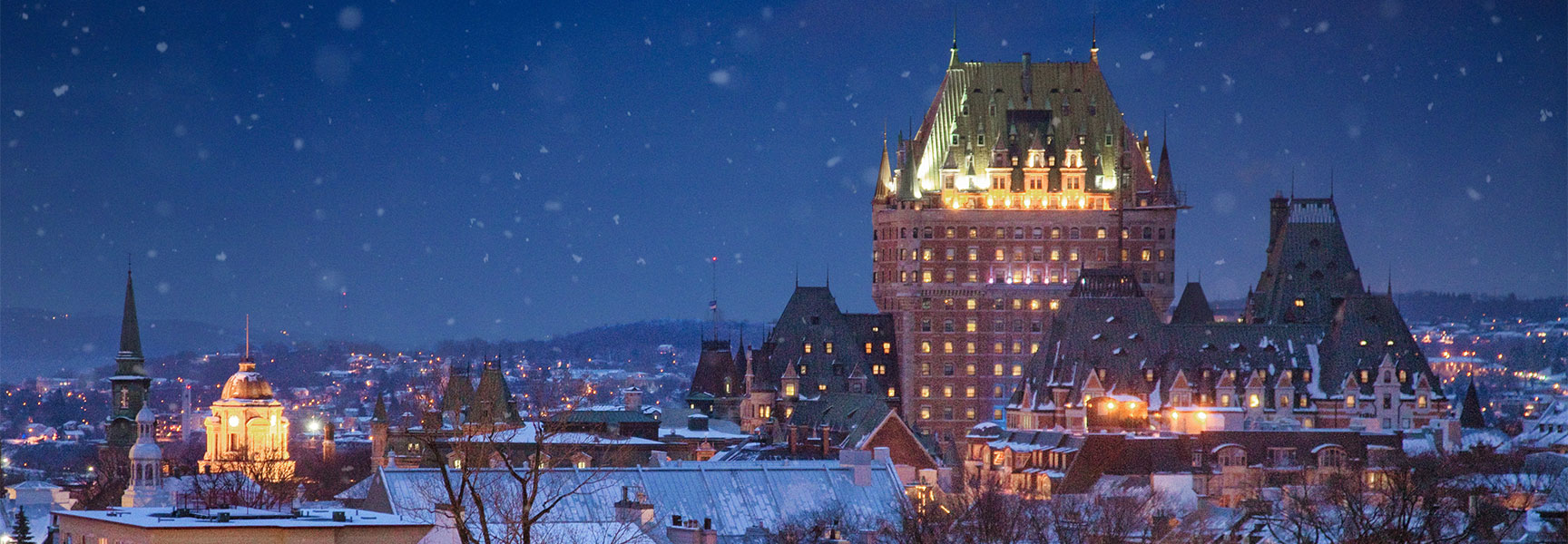 The grand Château Frontenac hotel in Québec illuminated at night as snow falls gently over the historic city.