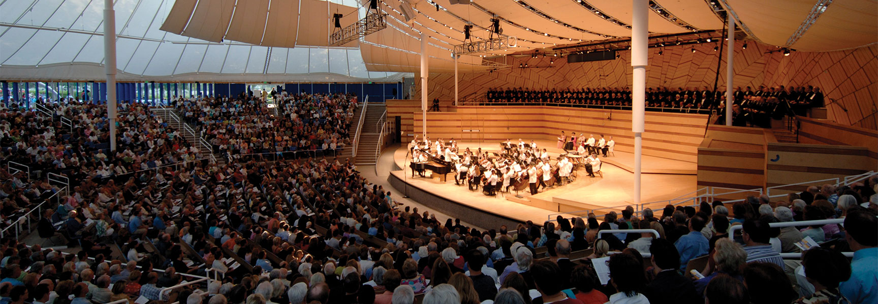 An orchestra and choir perform on stage for a large audience inside the Benedict Music Tent for the Aspen Music Festival in Colorado.