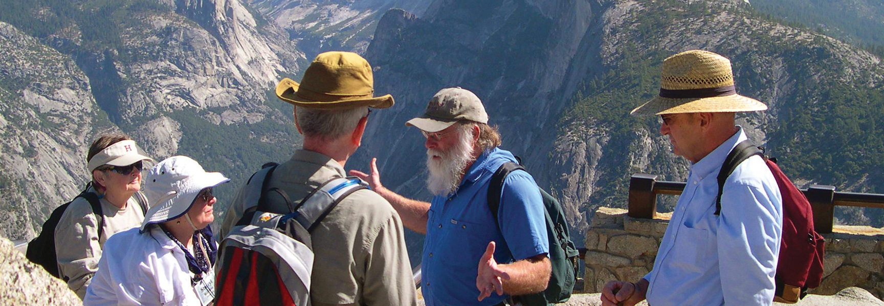 A group of hikers listens to a guide while overlooking a vast mountain valley in Yosemite National Park, California.