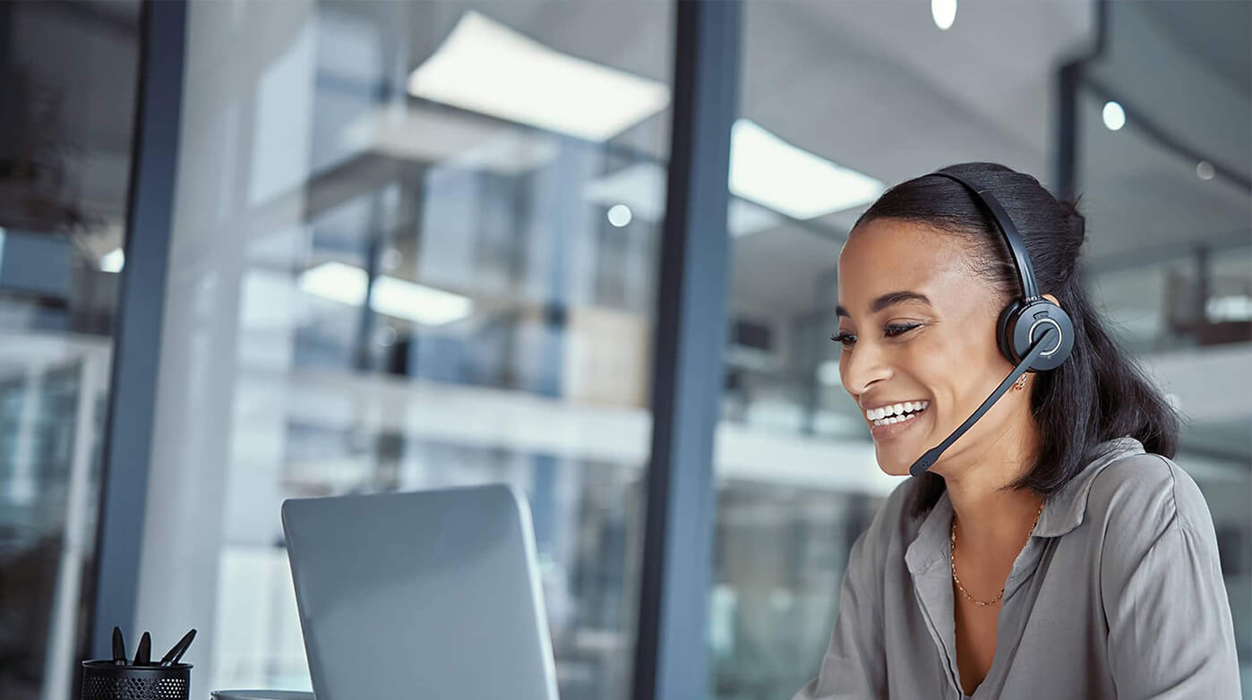 Side view of customer service agent wearing a headset and looking at a laptop.