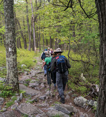 A group of hikers with backpacks and trekking poles walks along a rocky section of the Appalachian Trail in Pennsylvania's Pocono Mountains.