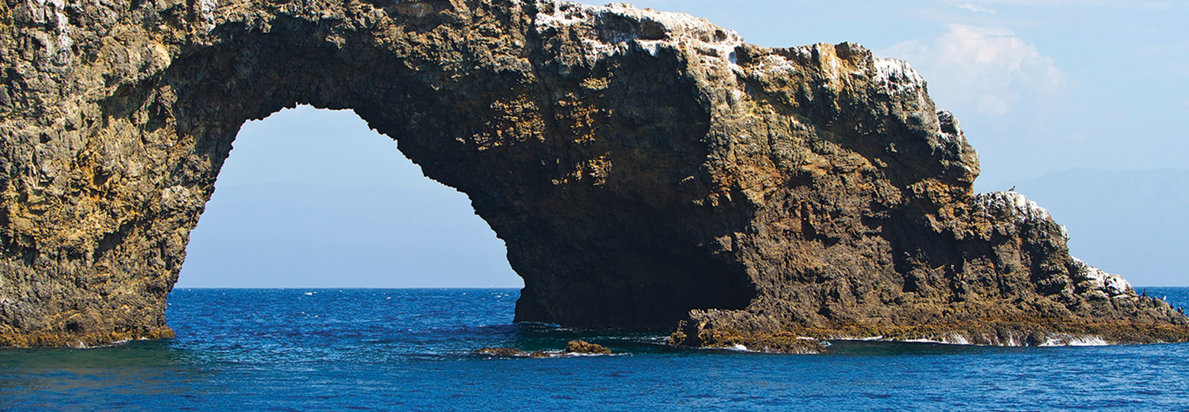 A large rock arch stands in the blue ocean at Channel Islands National Park in California.