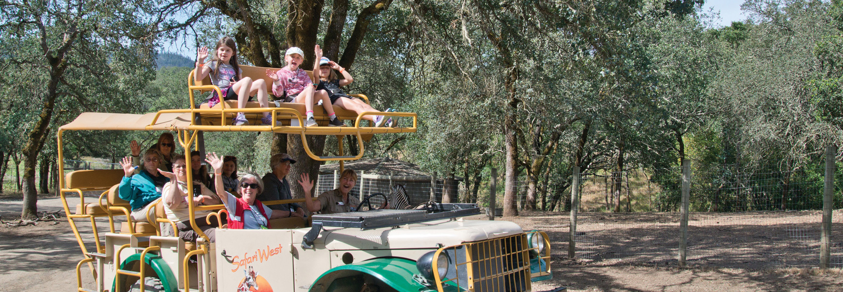A multigenerational group of people smile and wave from an open-air safari vehicle in Sonoma, California.