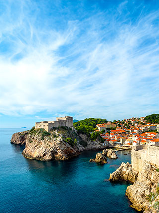 A view of the historic walled city of Dubrovnik, Croatia, on a rocky cliff overlooking the brilliant blue Adriatic Sea.