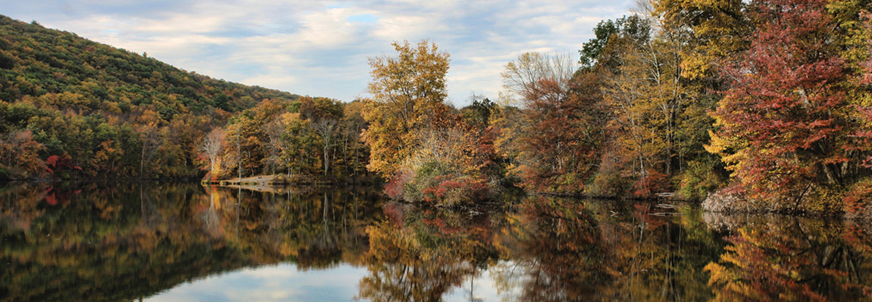 A scenic view of the Delaware River in the Poconos, Pennsylvania with colorful autumn trees reflected on the water's surface.