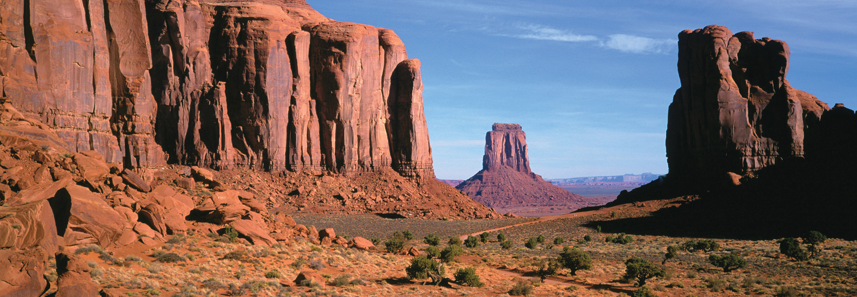 The iconic red rock buttes of Monument Valley in Arizona rise from the desert floor under a clear blue sky.