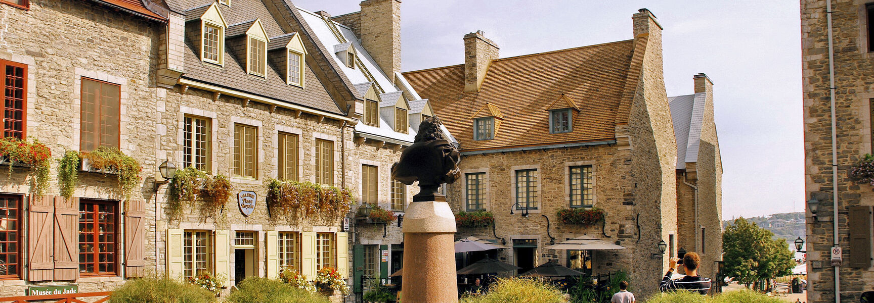 Historic stone buildings and colorful flower planters surround the cobblestone square of Place Royale in the Lower Town of Québec City.