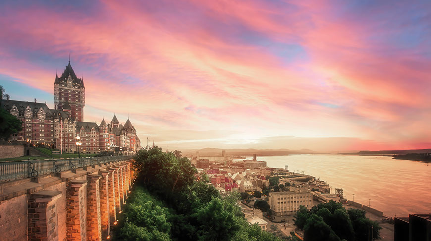 A pink sunrise glows over the iconic Château Frontenac and the historic architecture of Québec City overlooking the river.