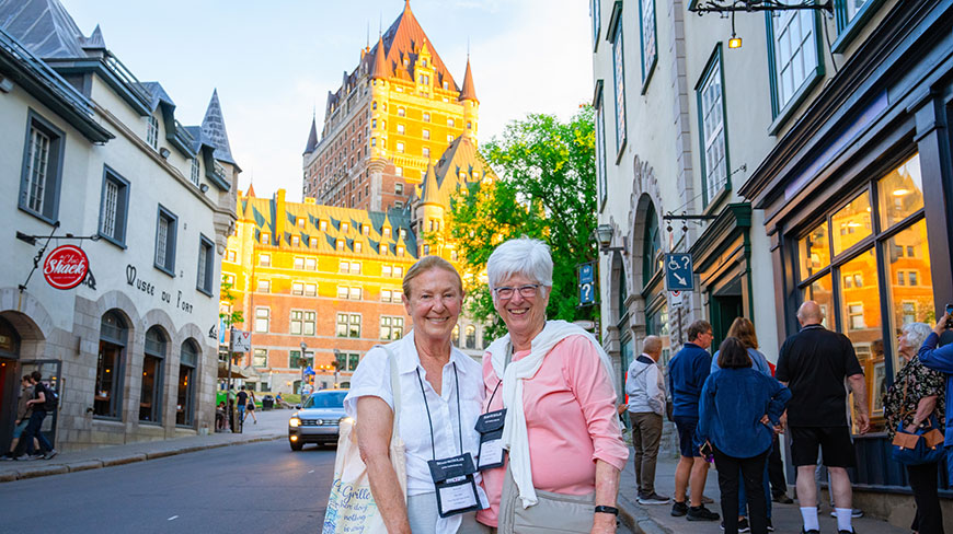 Two women smile on a street in Old Québec with the historic Château Frontenac in the background.