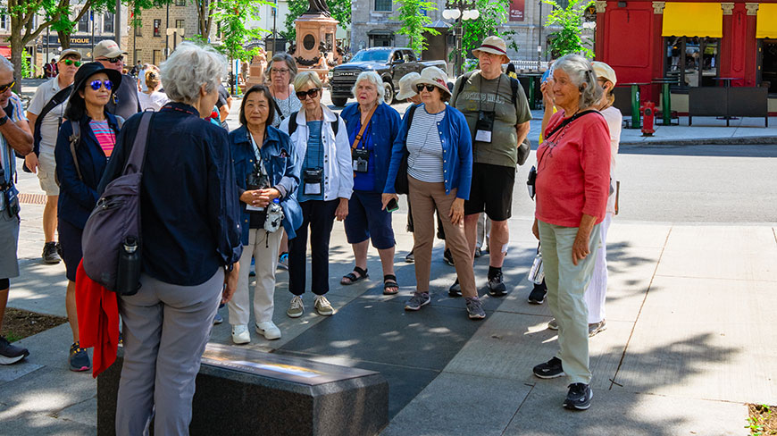 A group of travelers gathers outdoors to listen to a guide during a tour in the Old City of Québec.