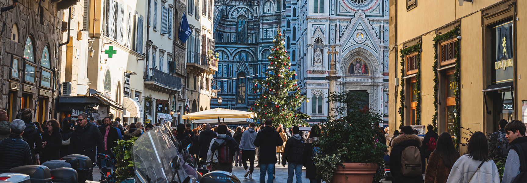 A crowded street in Florence, Italy, with a large Christmas tree in front of the ornate Duomo during the holiday season.