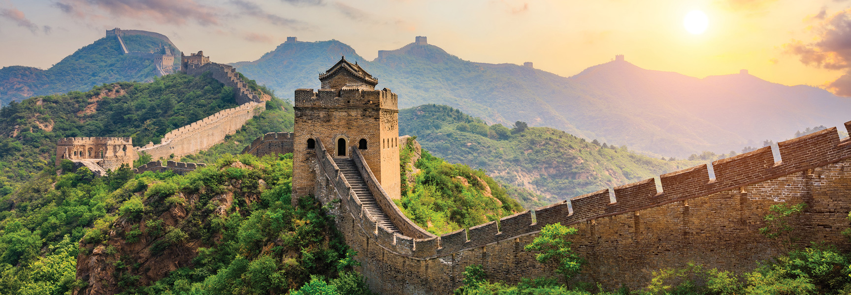 The Great Wall of China snakes across lush green mountains under a golden sunrise.