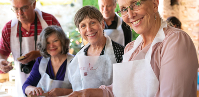 Smiling people wearing aprons participate in a Tuscan cooking class in Italy, preparing handmade pasta during a culinary adventure.