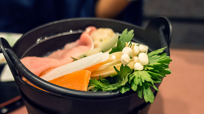 A Japanese hot pot meal from the Kisu Valley, with fresh vegetables, mushrooms, and meat arranged in a dark cast-iron nabe pot.