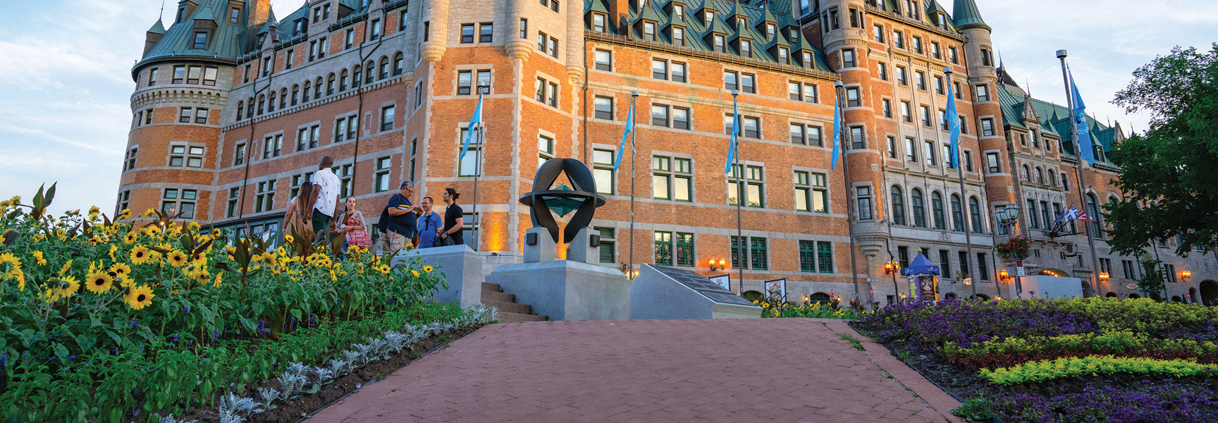 A group of people stand on a terrace with sunflower gardens in front of the grand, brick Château Frontenac hotel in Québec.