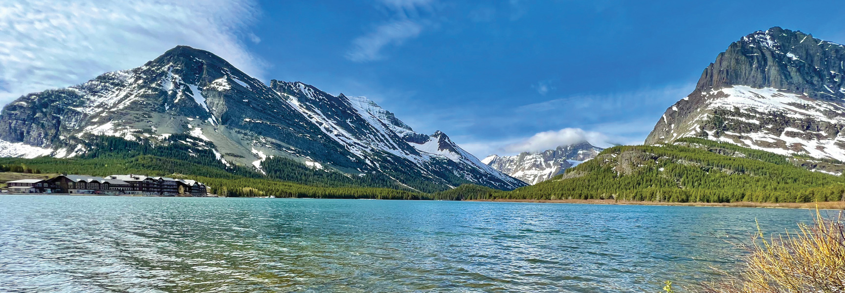 A historic lodge sits on the shore of a turquoise lake surrounded by snow-capped mountains in Glacier and Waterton Lakes National Parks.