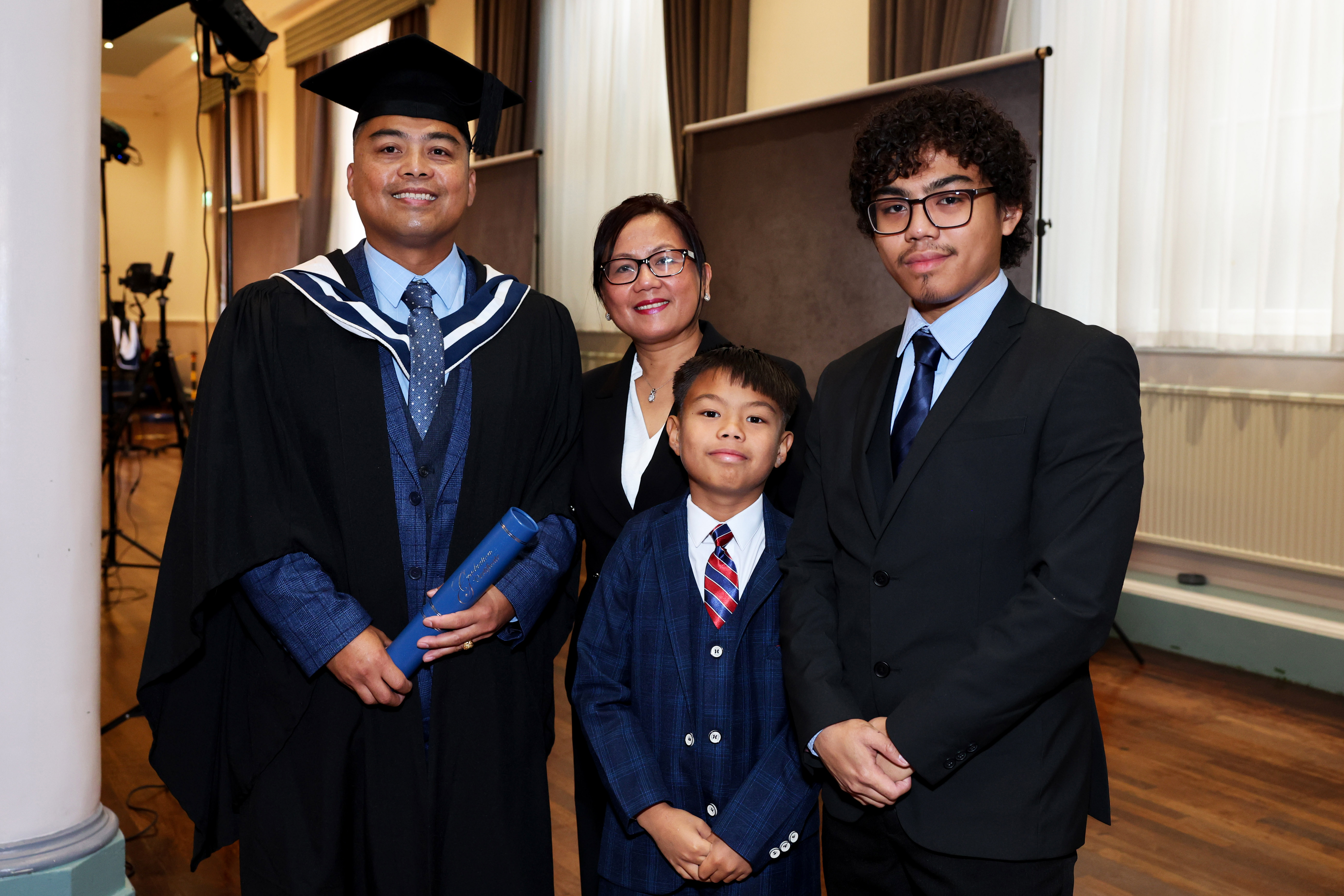 Male graduate in cap and gown posing with his partner and two children, one young one teenage age