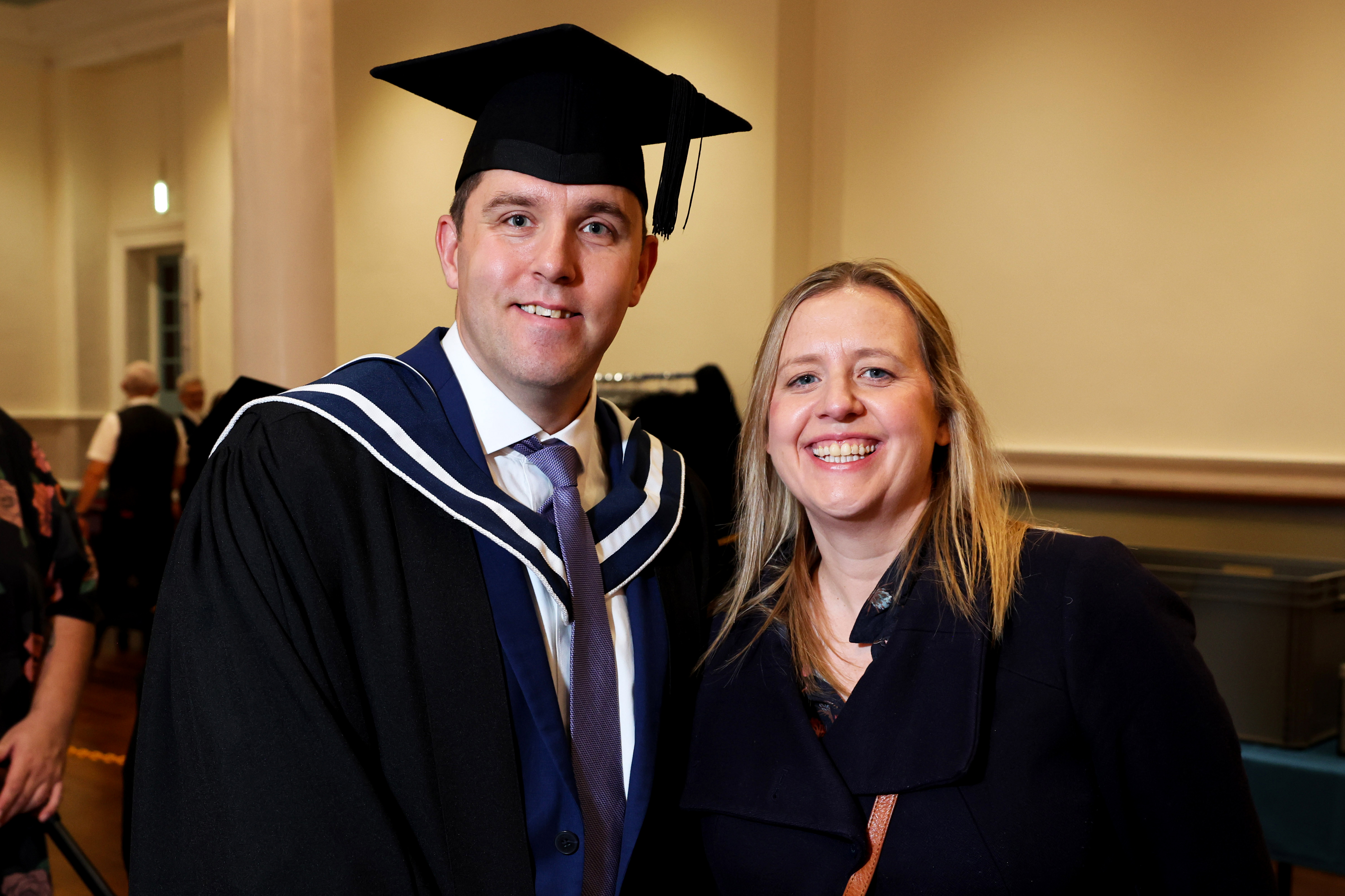 Male graduate in cap and gown posing with a woman (girlfriend, wife or loved one) after ceremony