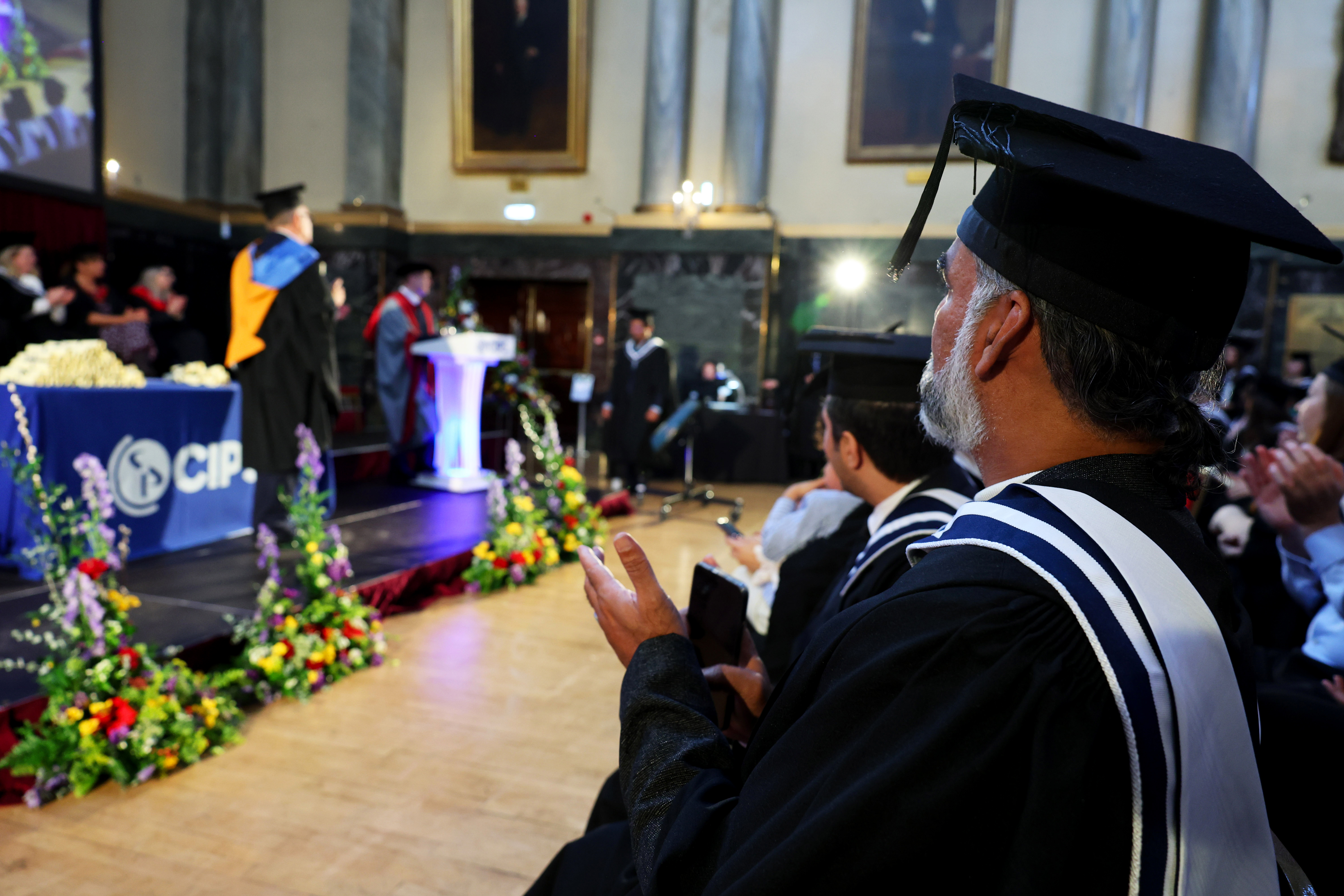 View of the stage with speakers, graduate in audience is clapping