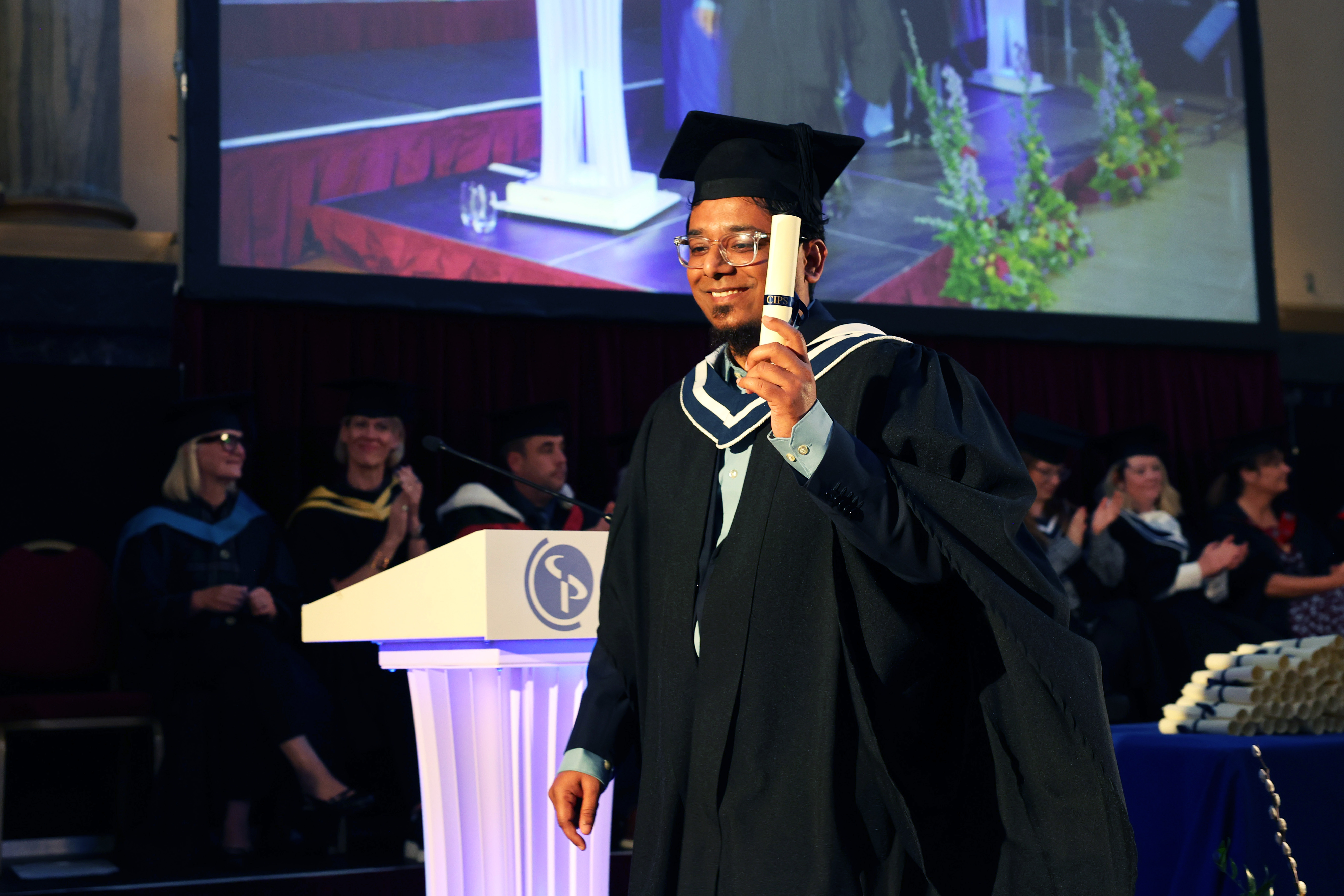 Male graduate in cap and gown holding diploma as he walks on the stage