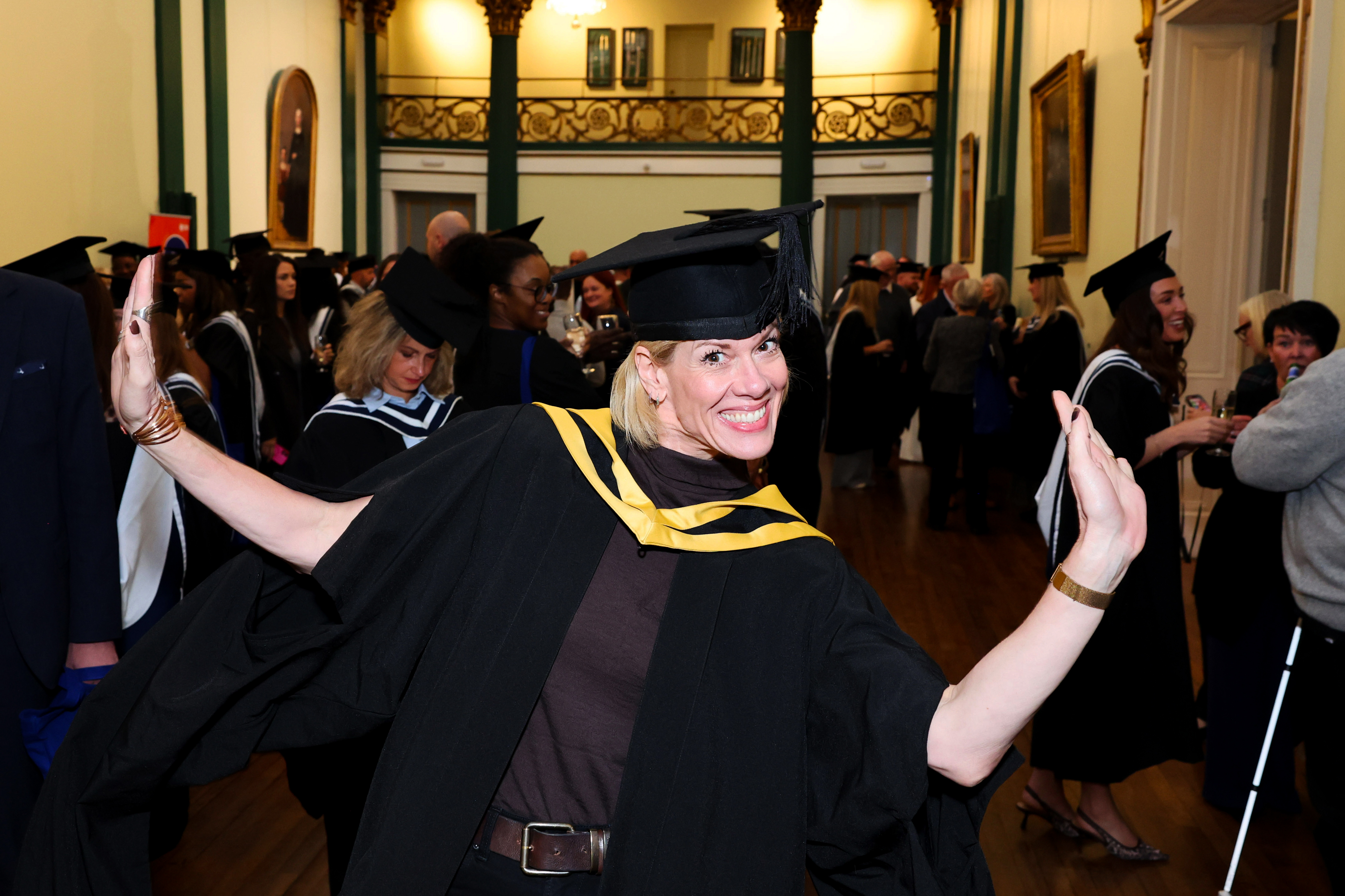 Female graduate in cap and gown strikes a funny pose after her graduation is complete, celebrating