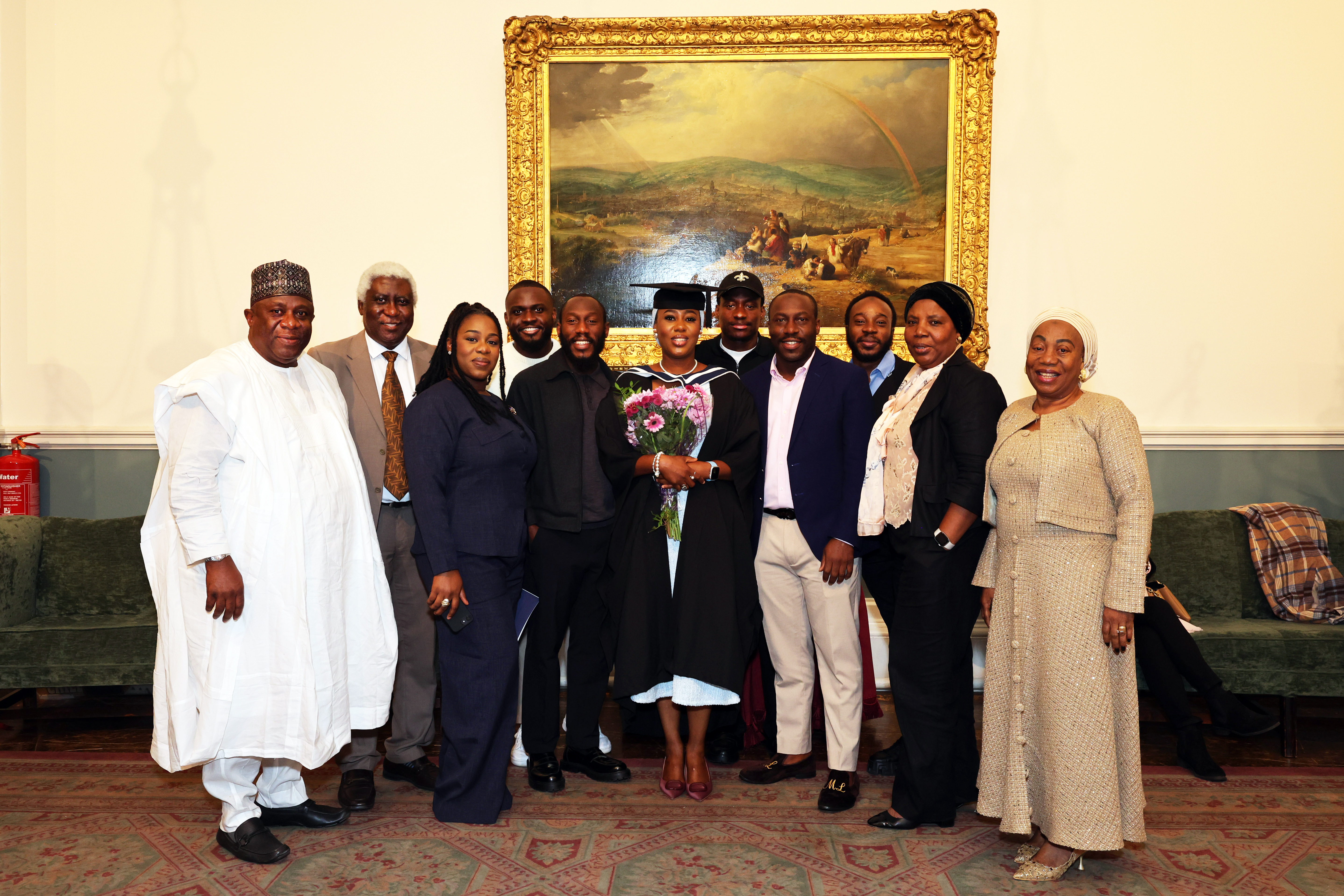 Female graduate in cap and gown is holding flowers and posing with a large group of 9 family members, looking very proud